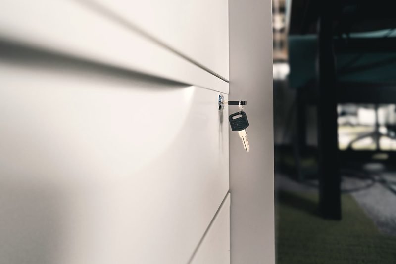 A small key in the lock of a white office cabinet