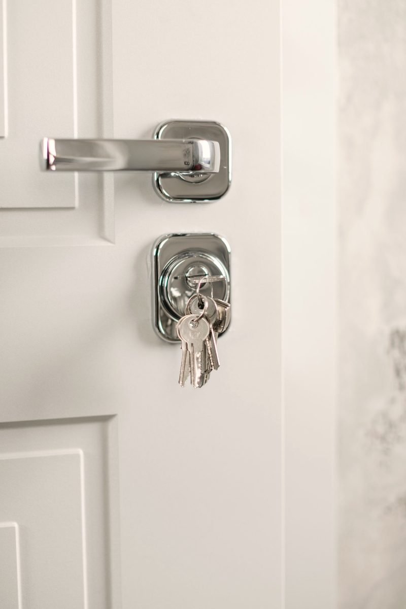 A chrome lever handle above a cylinder lock with keys hanging from it on a white door