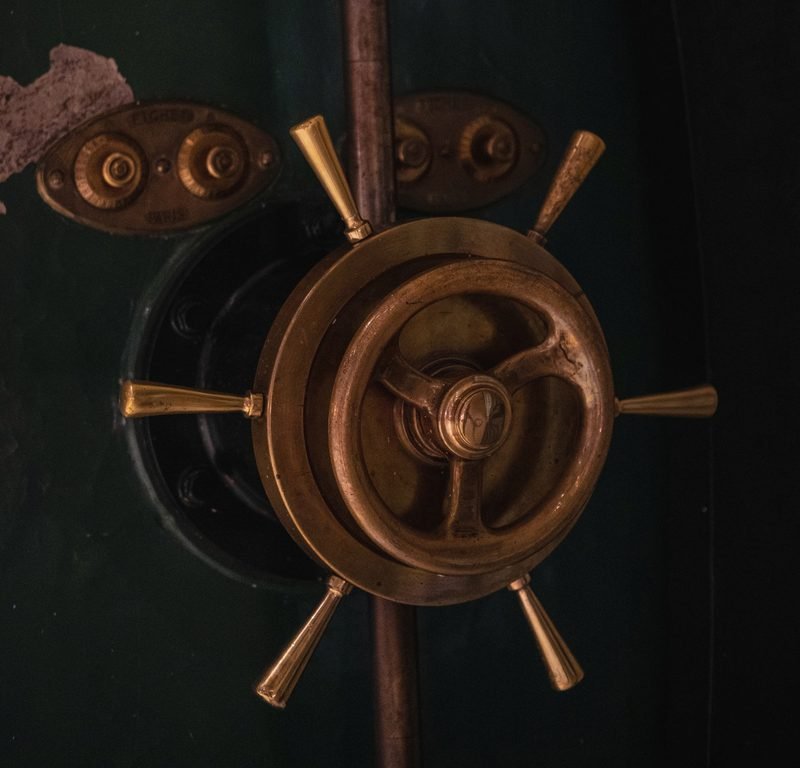 The brass spoked handle of an old dark green vault door